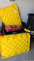 Yellow plastic storage bin with lid, partially opened. Mastercraft toolbox and extension cords inside.