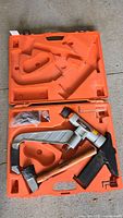 Paslode Floor Attack nailer and accessories neatly arranged inside orange molded plastic carrying case on a concrete floor.