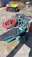 Photo showing red and green garden hoses coiled on ground with black splash guards and container in background.
