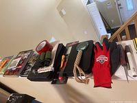 Full lot overview showing gloves, binoculars, cleaning products, and hand tools arranged on a ledge.