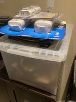 Stacked home electronics items on plastic storage bin against wall.