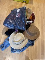 Photo of denim jacket, straw hats, and miscellaneous items including a basket with gloves and fleece hoodies on wooden floor.