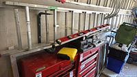 Full view of 32' aluminum extension ladder with yellow end covers leaning against wall above red tool chests.