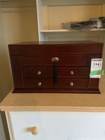 Front view of large wooden jewelry box with lock and tassel key, three drawers visible