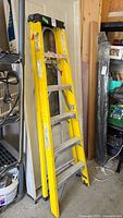 Yellow heavy duty step ladder folded against wall in garage.