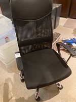 Front view of black mesh office chair with cushioned seat and armrests visible.