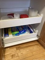Drawer with multiple plastic food containers and lids, boxes of plastic wrap, aluminum foil, and Ziploc storage bags beneath.