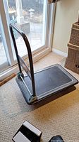 Photo showing the full platform cart with metal handle and rubberized platform surface placed on carpet near sliding door.