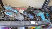 View of several blue power tools including a Makita angle grinder and Mastercraft tool laid on a bench, cords visible, showing dust and use wear.