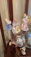 Photo of three Royal Albert Old Country Roses figurines of girls with floral dresses and animals inside a wooden and glass display cabinet.