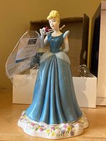 Front view of Cinderella figurine in blue dress holding a rose, with box in background.