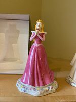 Figurine of Sleeping Beauty in a pink gown with floral base, next to an open box.