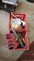 Full view of two red crates containing assorted hand tools, safety ear protectors, and a halogen lamp