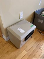 Full view of beige/gray Sentry 1170 safe on wooden floor near wall outlet.