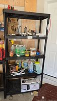 Full view of black plastic shelving unit with items on shelves, showing four shelves and cylindrical support legs.