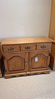 Front view of wooden sideboard cabinet showing three drawers and two cabinet doors with brass handles and hinges.