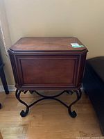 Full view of the wooden storage chest table showing the rectangular chest with a hinged lid and metal base with curved legs.