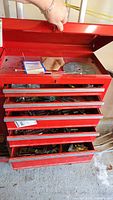 Photo showing full red tool chest with drawers open revealing various hand tools and accessories inside.