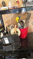 Black tool bag with hand tools on table with red bucket containing additional tools and supplies