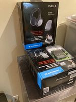 Stacked boxed sets of Sennheiser wireless headphones including RS 116 II model with wireless base station and Piezo RX Bluetooth headphones packaging on top.