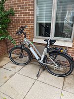 Side view of entire silver step-thru electric bike on kickstand showing frame, battery, rack and lights