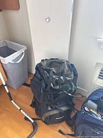 Large green and black Explorer 4000 backpack with multiple straps and buckles, standing upright on wooden floor with white wall background.