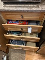 View of open kitchen drawers showing plastic wrap boxes in upper drawer and baking/roasting pans in lower drawers.