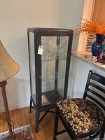 Full view of the tall metal and glass display cabinet, showing glass door, two internal glass shelves, and overall structure.