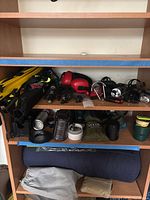 Shelving unit with assorted camping equipment: flashlights, headlamps, hammock pouch, yellow hiking poles, ropes, canisters, and containers.