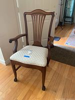 Front angle view of wood armchair showing carved fan backrest, armrests, and light beige upholstered seat with wear and stains.
