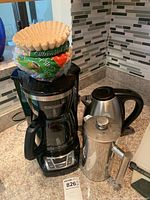 Black & Decker coffee maker, stainless steel coffee press, and electric kettle on kitchen counter with coffee filters on top of coffee maker.