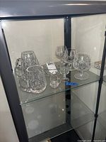 Wide view of Waterford crystal set on glass shelf, showing mugs, snifters, shot glass, ashtray and miniature glass.