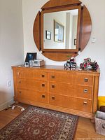 Front view of the light brown wooden dresser with six square-handled drawers and large round mirror.