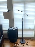 Full view of floor lamp next to window showing black arched arm and beige drum lampshade.