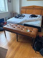 Angle view of the wooden foot bench in bedroom setting showing the tufted leather top and nailhead trim.