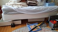 Side view of Ikea bed with white mattress and under-bed drawers, part of mattress sheet pulled back.