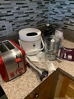Overview of three kitchen appliances on countertop: Cuisinart toaster, white Mischcdea cooker, Breville hand blender with accessories and manual.