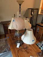 Photo showing all three table lamps with various fabric shades and one pink decorative glass globe shade on a dining table.
