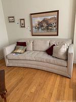 Beige Martha Stewart sofa with curved seat cushion and multiple pillows against wall with paintings above. Shows wear and tear on fabric.