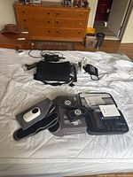 Wide view of all items on bed including Nooro leg massager, Hometech massager in case, blood pressure monitor, flashlight, jump rope, and seat pad.