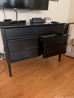 Full view of black media cabinet showing its four drawers, with the right bottom drawer open revealing storage space suitable for files.