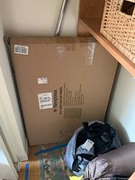 Photo of boxed Newpowa off-grid solar panel placed against a wall in a narrow space beside furniture and bags.