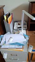 View of the top of filing cabinet showing paper materials, stapler, calculator, desk lamp and organizer tray.