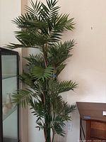 Full height view of the faux palm plant showing the upper green fronds and the brown stems.