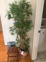 Full view of the tall faux bamboo plant inside the planter placed on wooden floor near a chair.