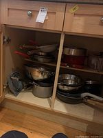 Wide view of cupboard with assorted pots, pans, mixing bowls, and colanders.