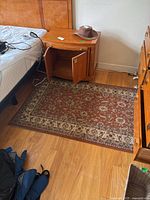 Photo of rectangular Agra runner rug on hardwood floor next to a bed, showing traditional design with floral and geometric patterns in brown and cream tones.