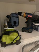Ryobi blue and silver circular saw and blue cordless drill with green charger on white shelf
