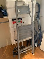 Front view of silver metal step ladder leaning against furniture, showing four steps and wear spots.