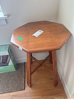 Front and side view of wooden octagonal side table with medium brown finish, placed on hardwood floor near a wall corner.
